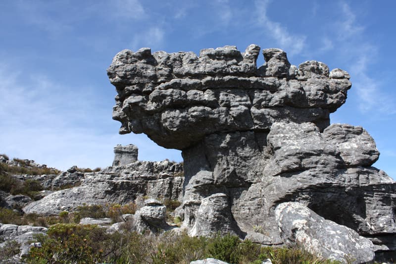 Verwitterte Sandsteinblöcke auf dem Plateau, unten schmal ausgewaschen und oben breit, darüber blauer Himmel