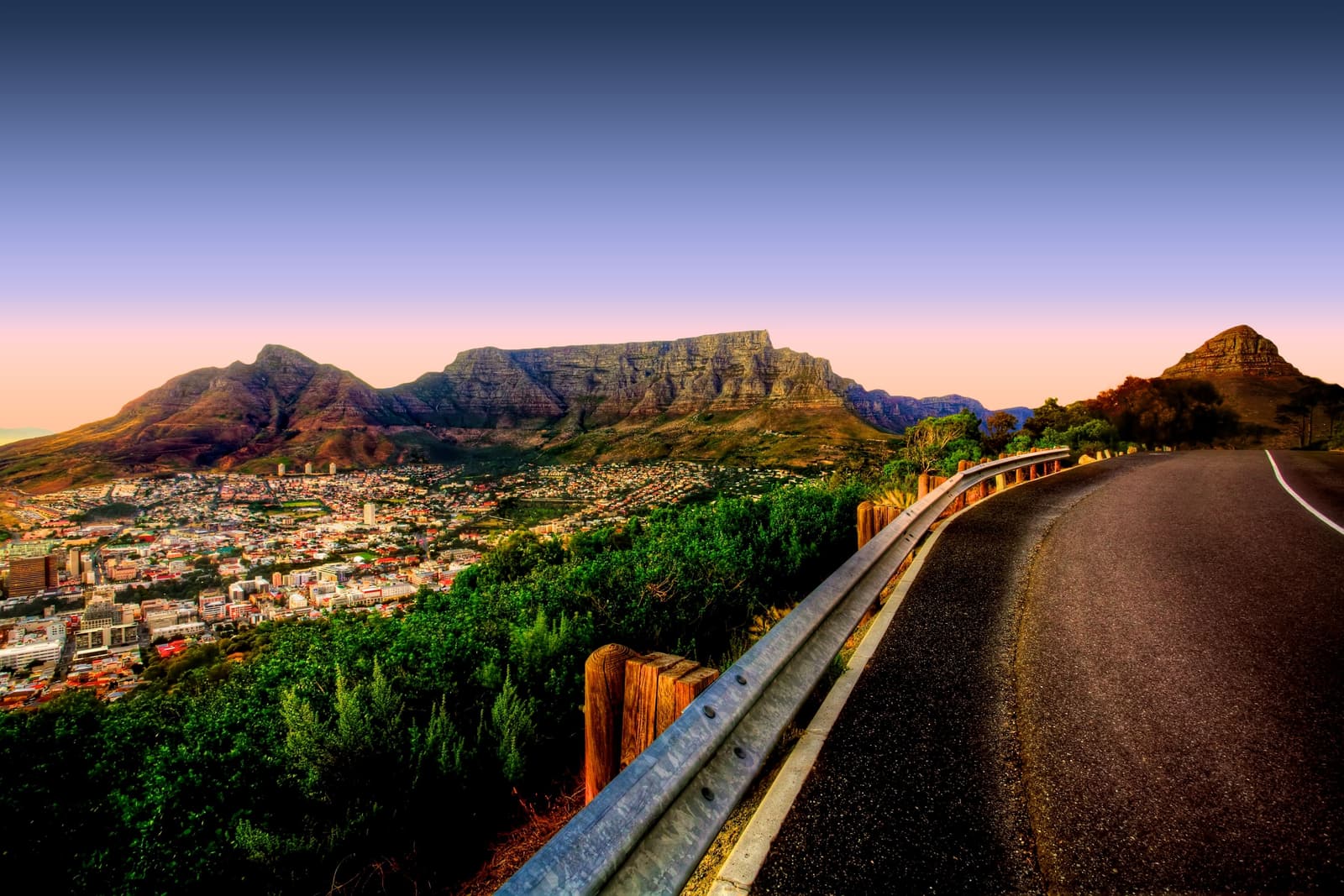 Straße am Signal Hill in der Dämmerung, dahinter die Lichter der Stadt, der Tafelberg und Lion's Head