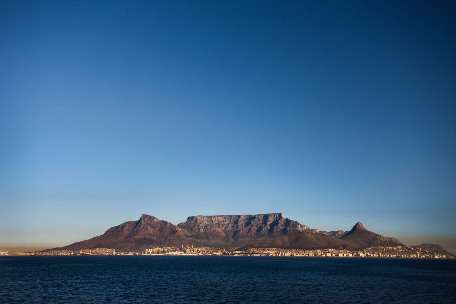 Der Tafelberg als dunkle Silhouette über dem Wasser der Tafelbucht in der Dämmerung